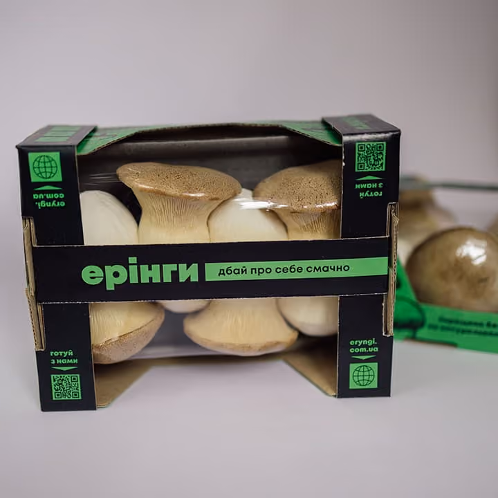 Box of fresh king oyster mushrooms with green and black packaging labeled in Ukrainian text.