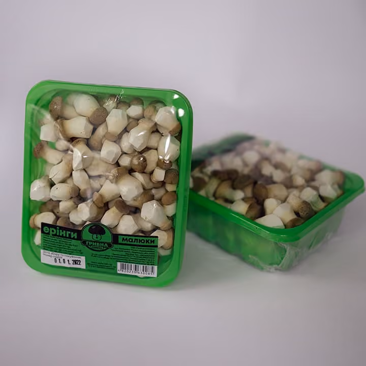 Two green plastic containers of small white mushrooms with brown caps on a white surface.