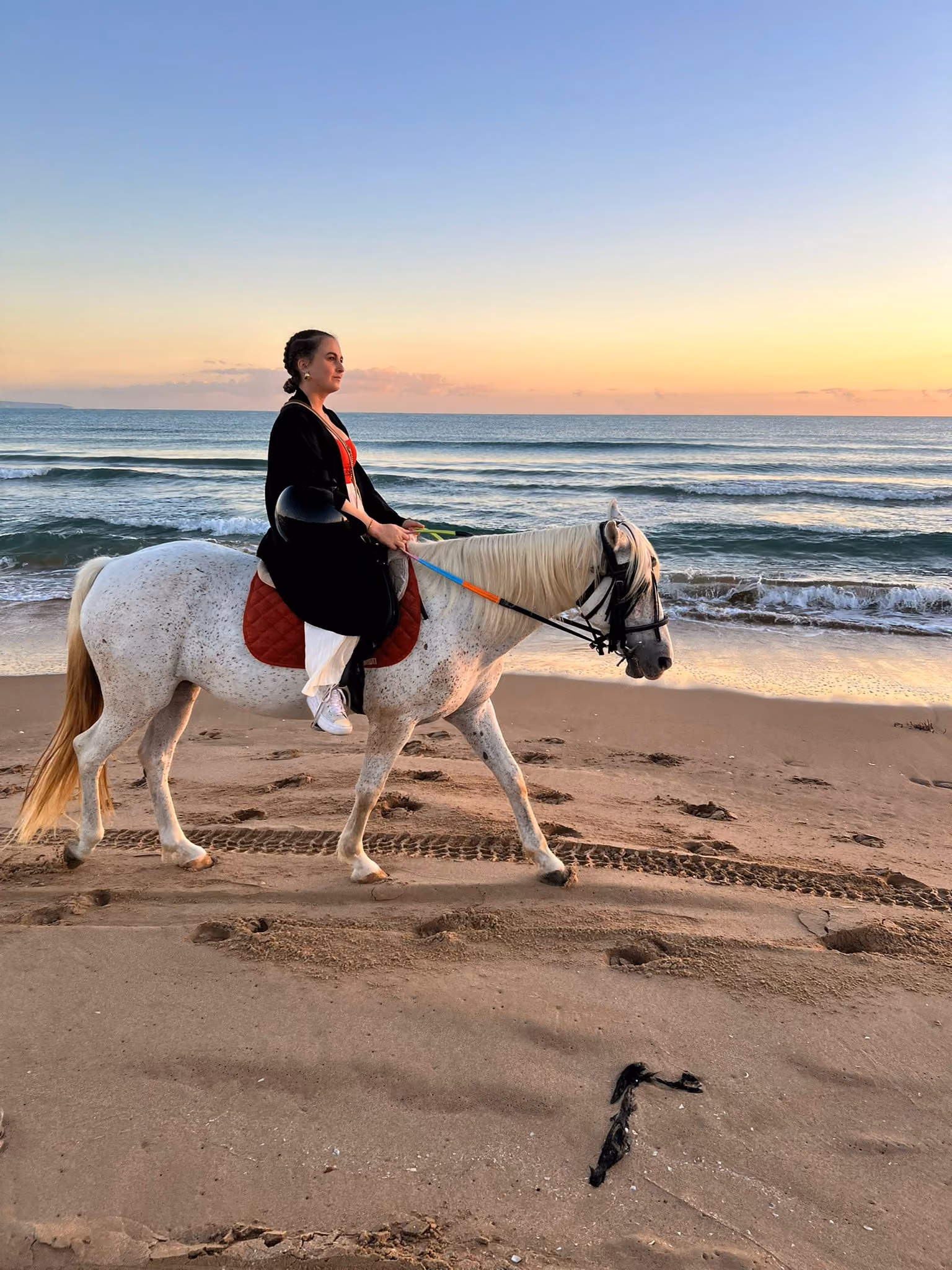 Une femme qui se balade à cheval sur la plage, lors d'un levé de soleil au Maroc. Une expérience Casaniyya