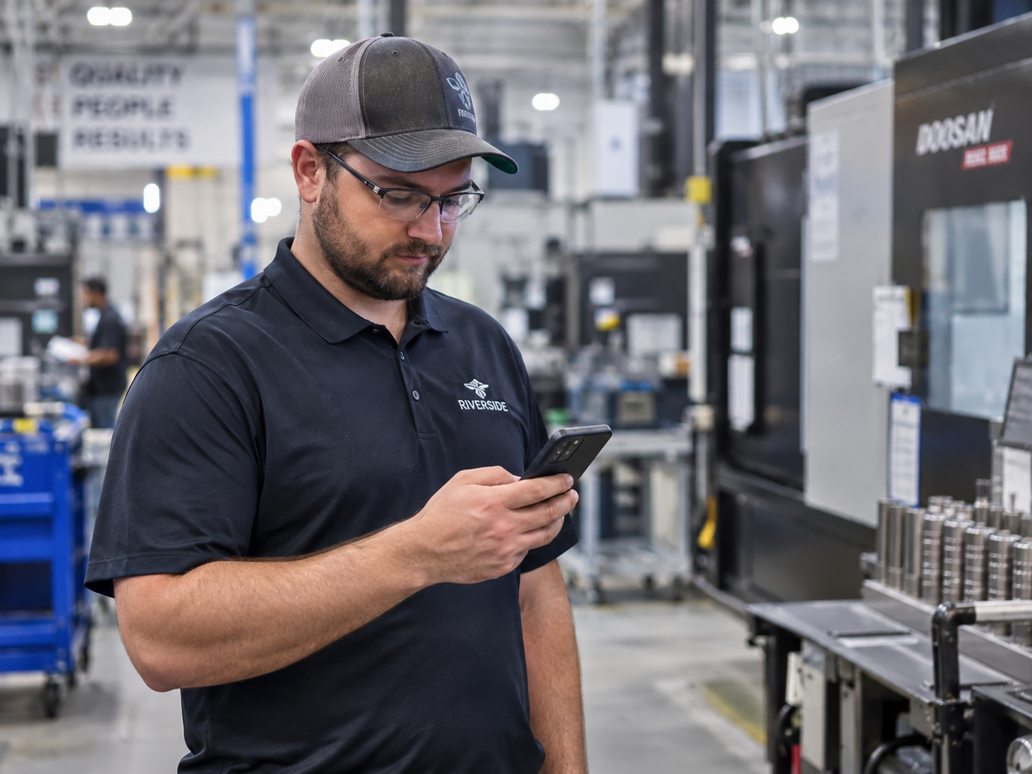 A frontline manufacturing employee reads a shift offer text on his phone on the plant floor