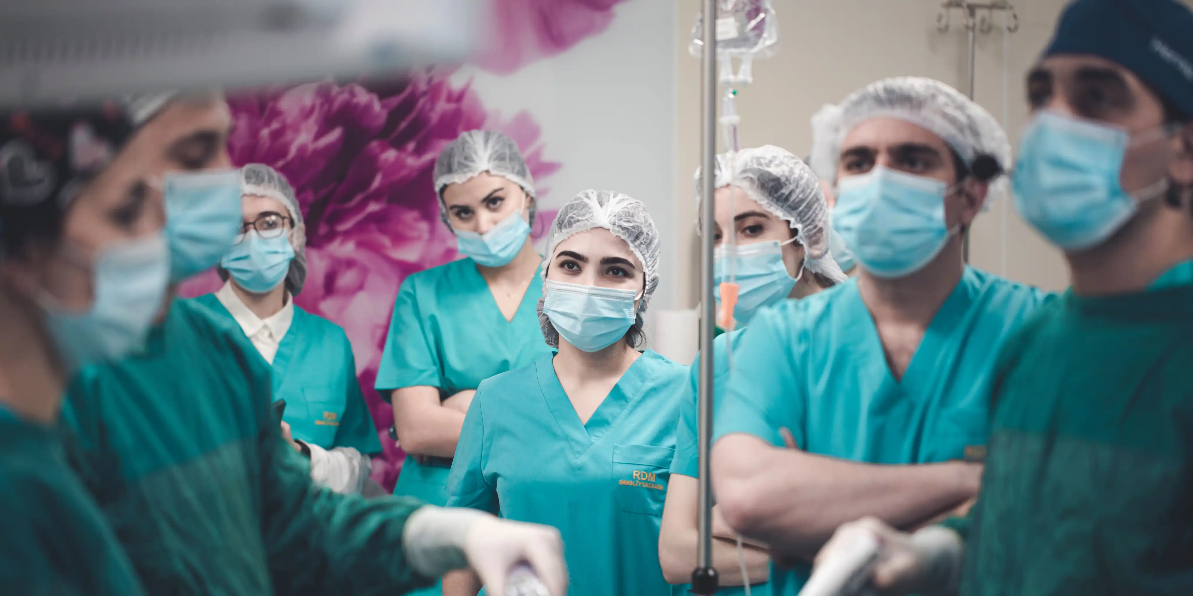 Group of medical staff wearing scrubs, hairnets, and masks in a hospital setting.