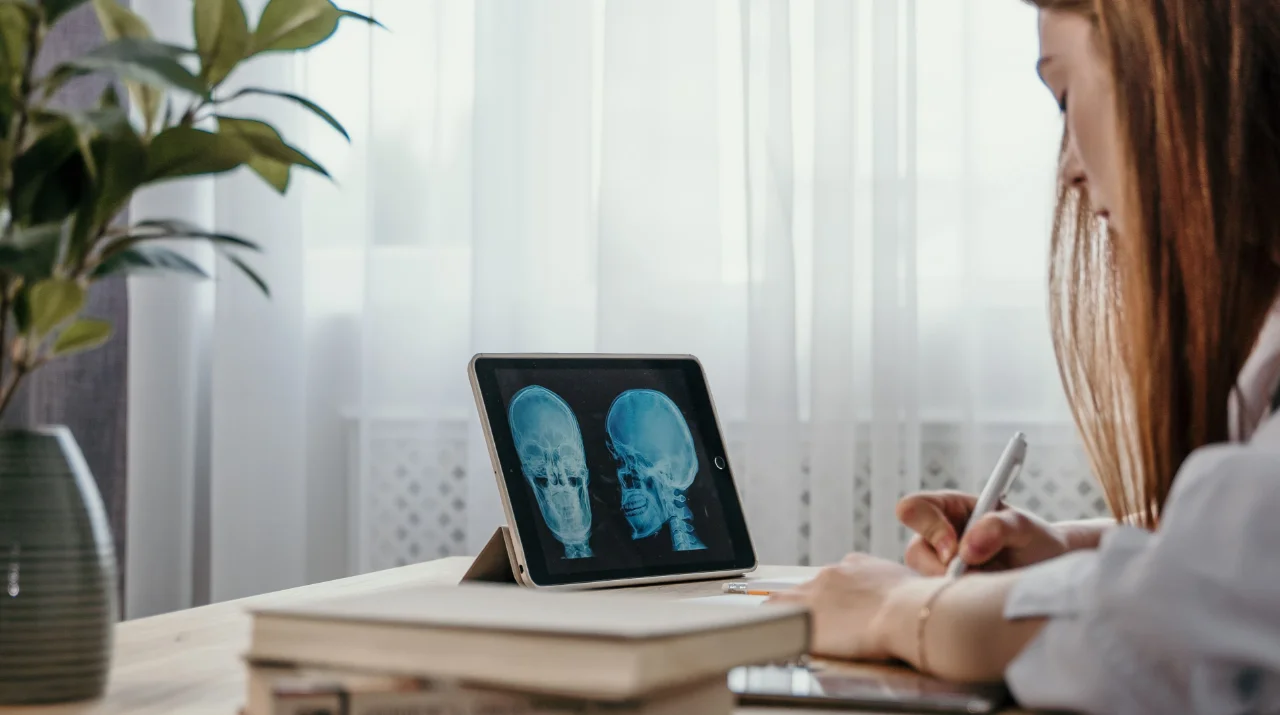 Woman sitting at a desk studying skull X-rays displayed on a tablet in a softly lit room.