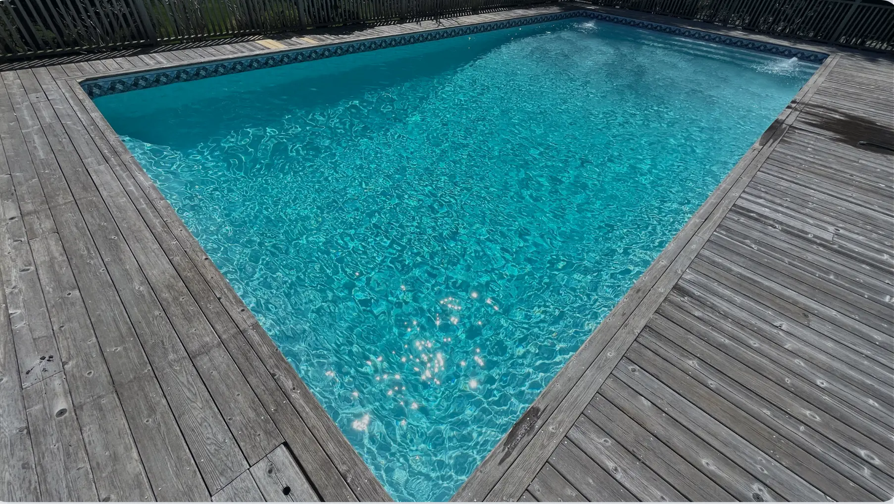 Clear blue swimming pool with rippling water surrounded by a weathered wooden deck and fenced by vertical wooden slats in Westhampton Beach.
