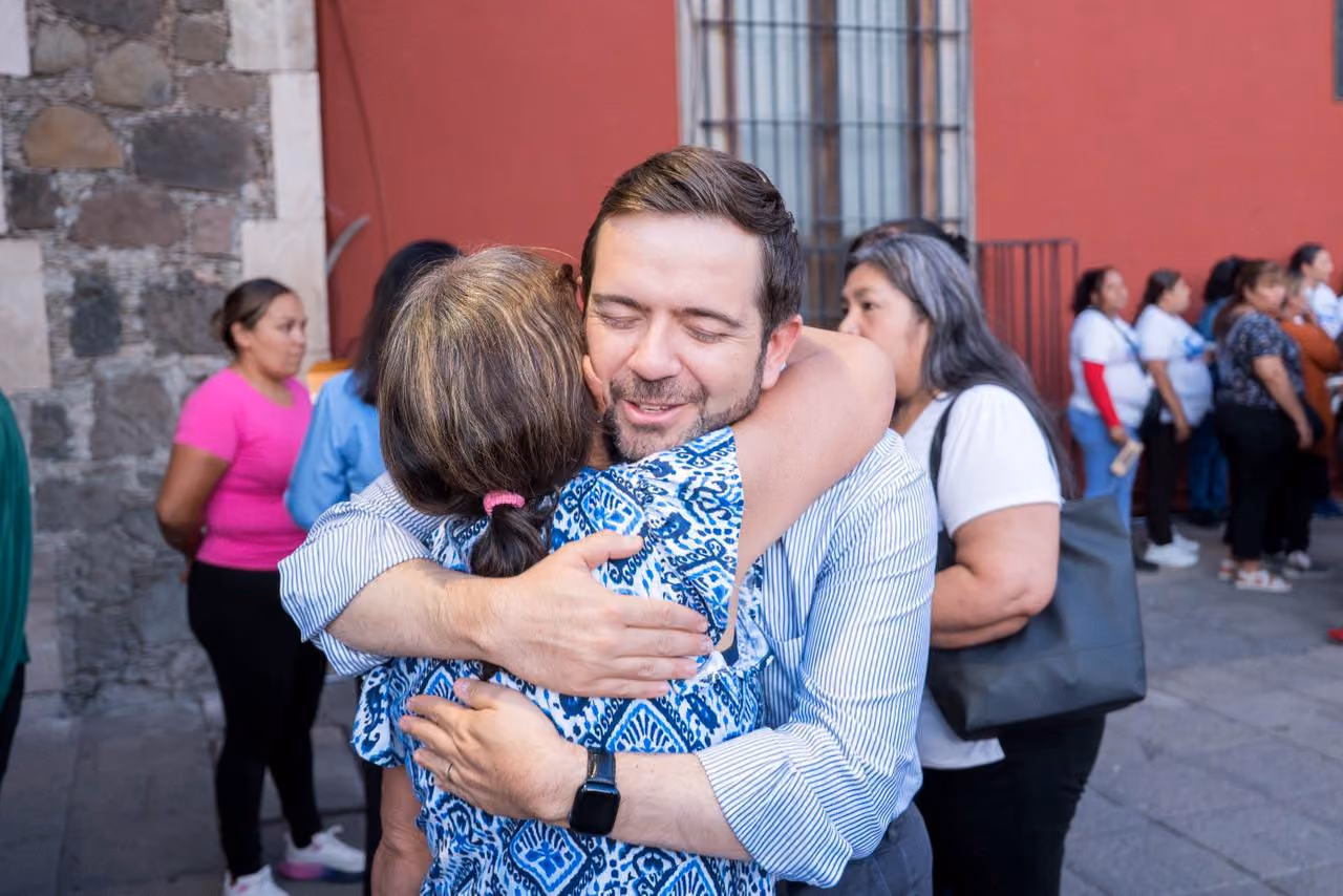 Man and woman warmly hugging outdoors with other people blurred in the background.