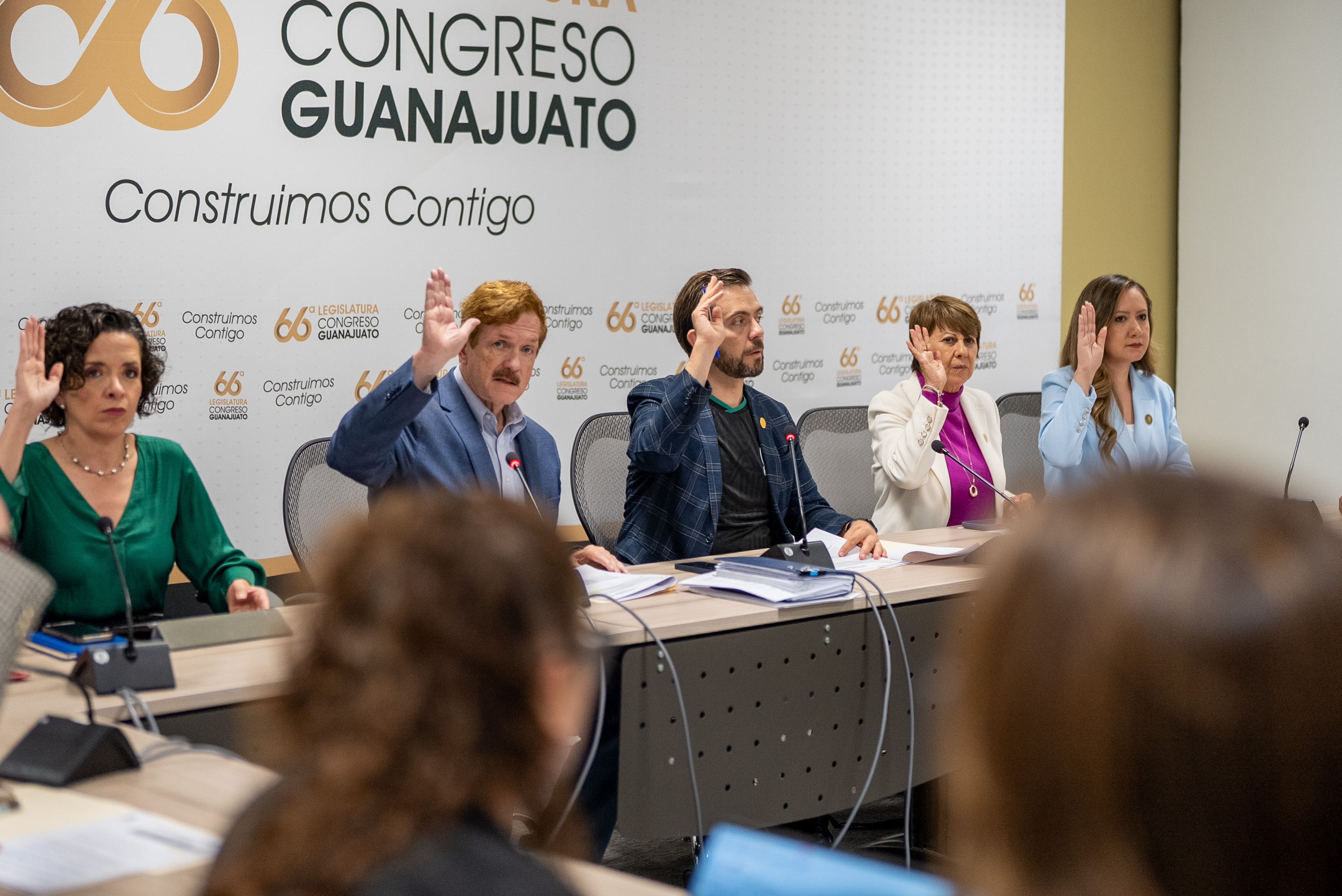 Five people seated at a conference table raising their hands in a meeting room with Congreso Guanajuato signage.