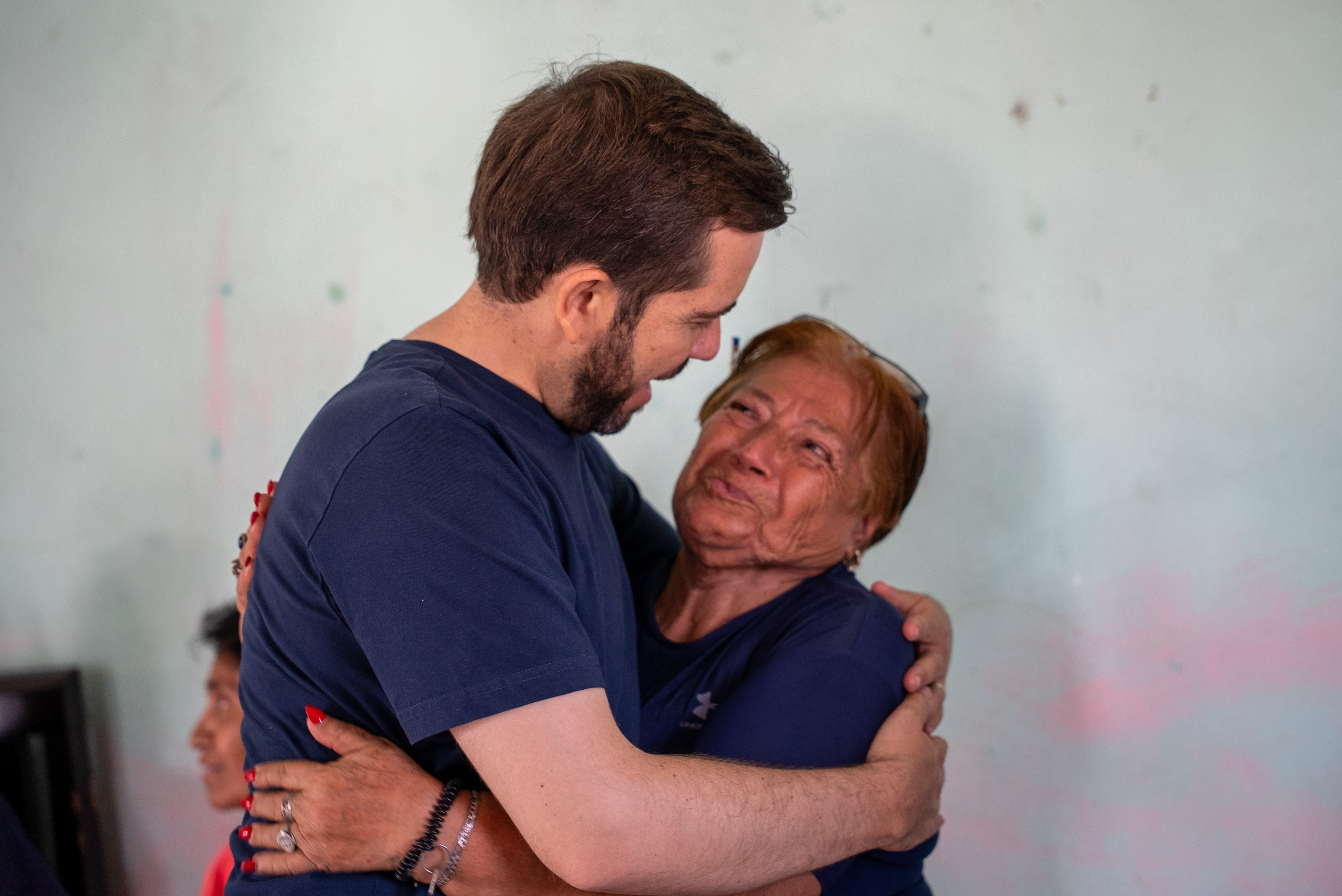 A man and an older woman warmly embrace indoors, sharing a joyful moment.