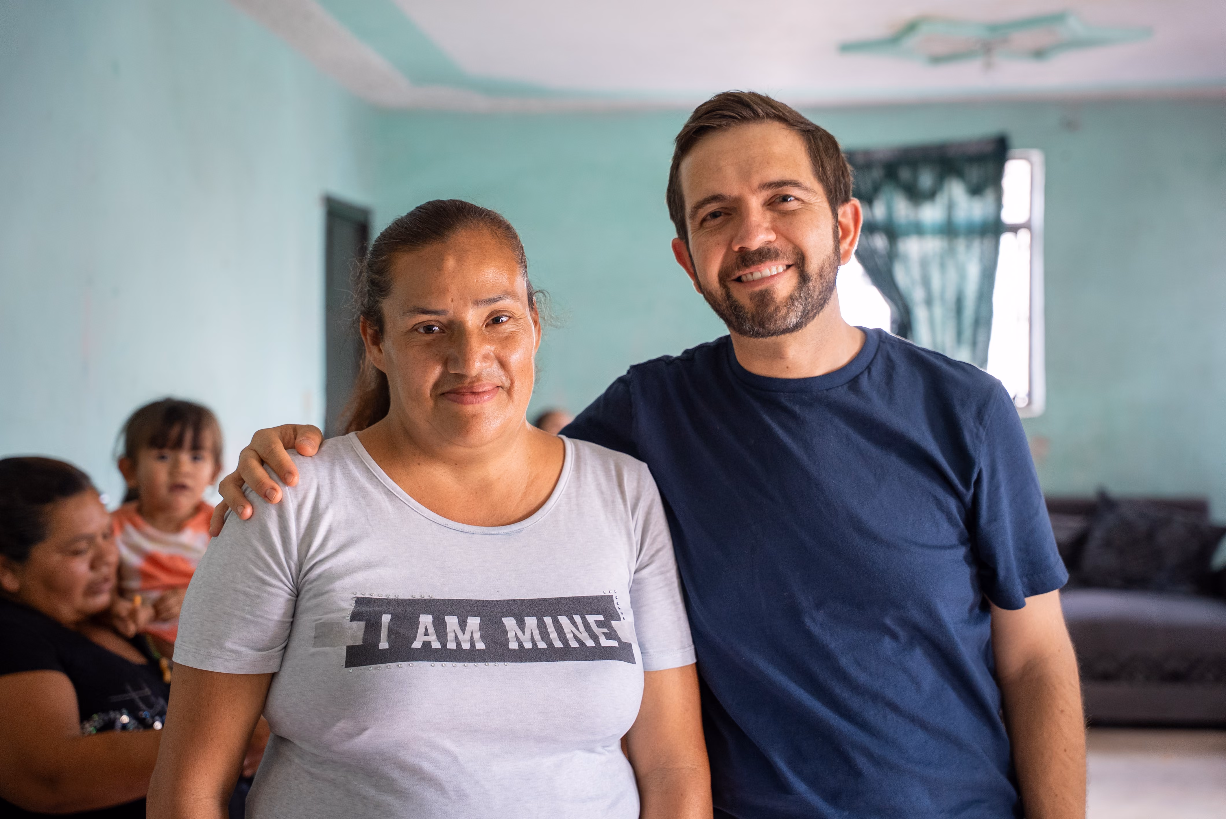 Smiling man in a blue shirt with his arm around a woman wearing a white shirt reading 'I AM MINE'.
