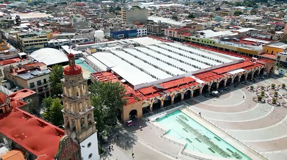 Aerial view of a large historical building with red roofs, arches, and a bell tower in a city.
