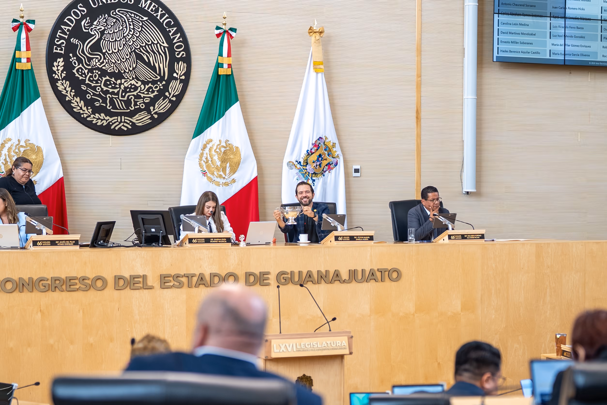 Officials seated at the Congress of Guanajuato with Mexican flags and a large emblem behind them.