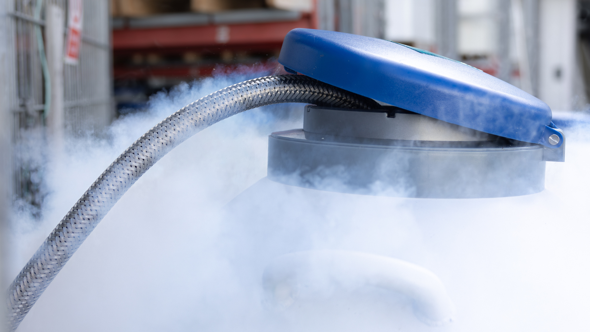 Close-up of a blue-lidded container with a hose releasing white vapor or gas.