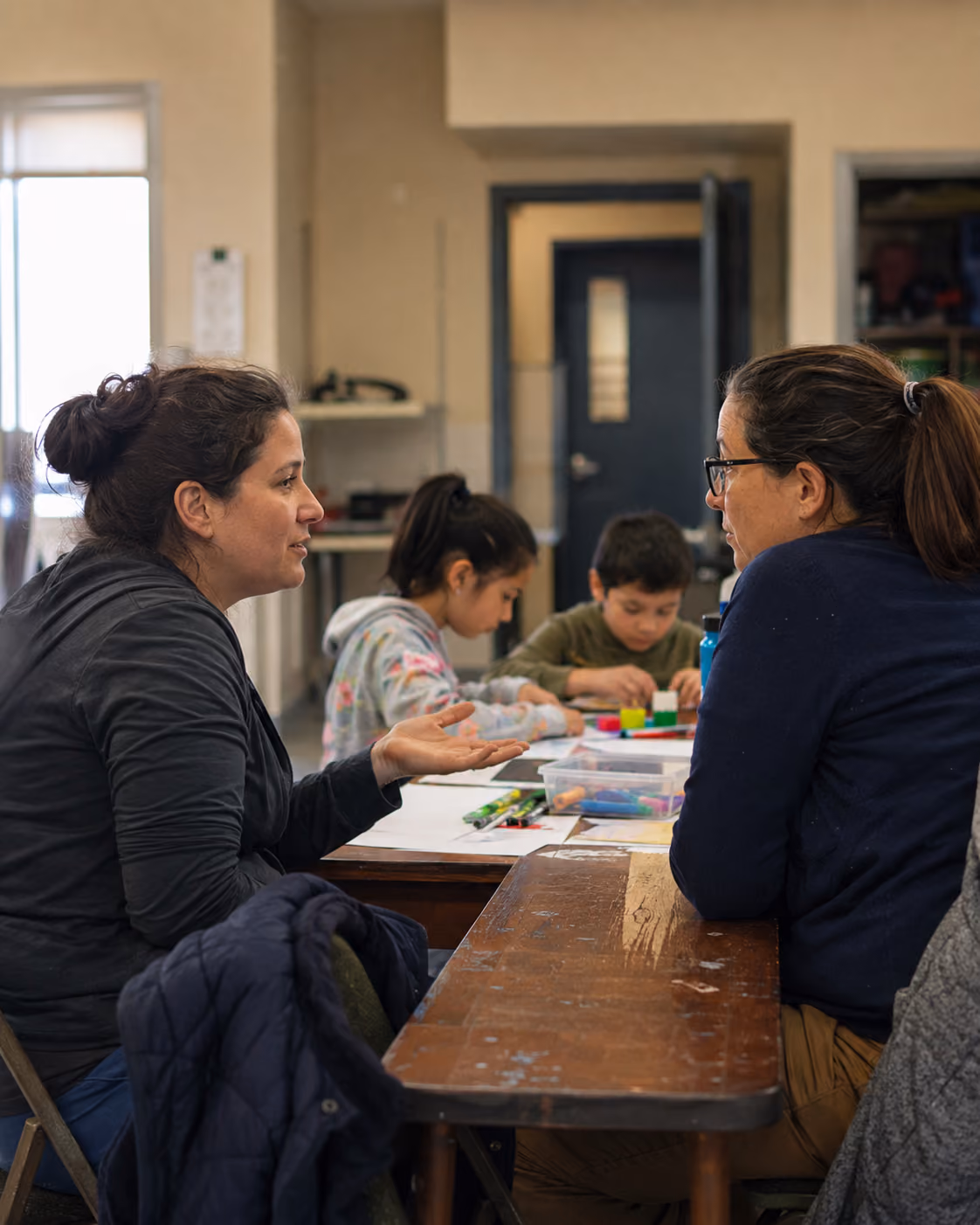 A parent and community facilitator talking while children take part in an activity