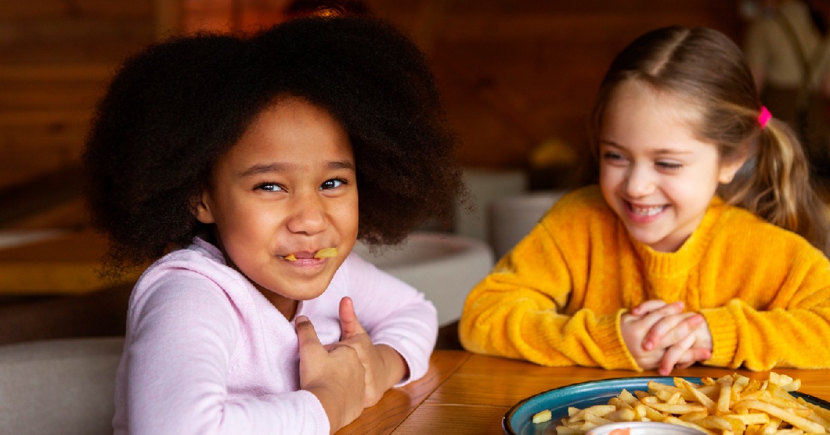 Meninas felizes comendo batatas fritas - Dia das Crianças em restaurantes