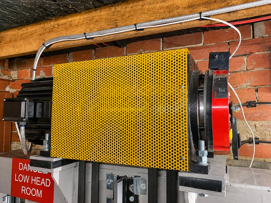 Guarded geared traction machine on a brick wall, with low head room warning signage