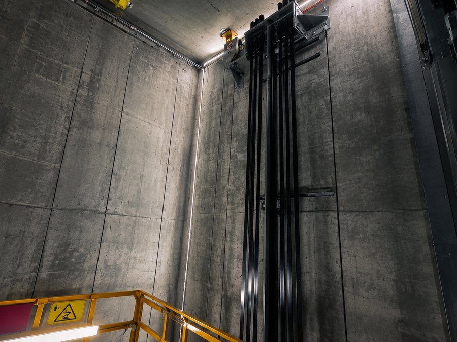 A lift shaft under construction, with bare concrete walls and guide rails installed