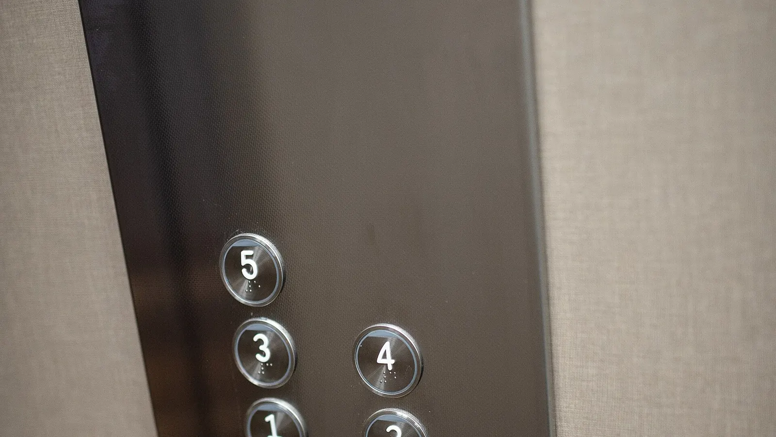 Close-up of a lift car push-button panel, the round floor buttons numbered one to five with braille beneath each number