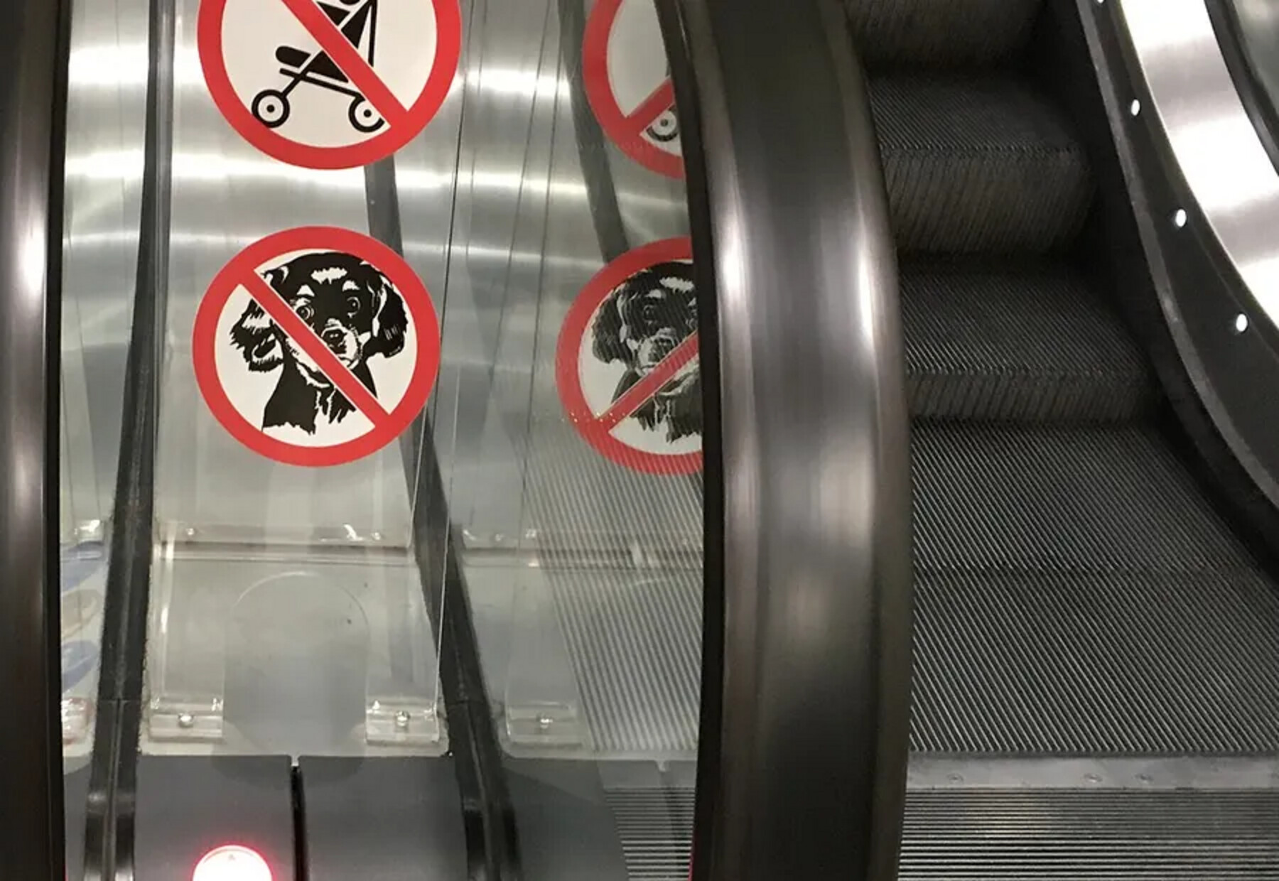 Two dog prohibition decals and a pram decal fitted to the glass balustrade of an escalator
