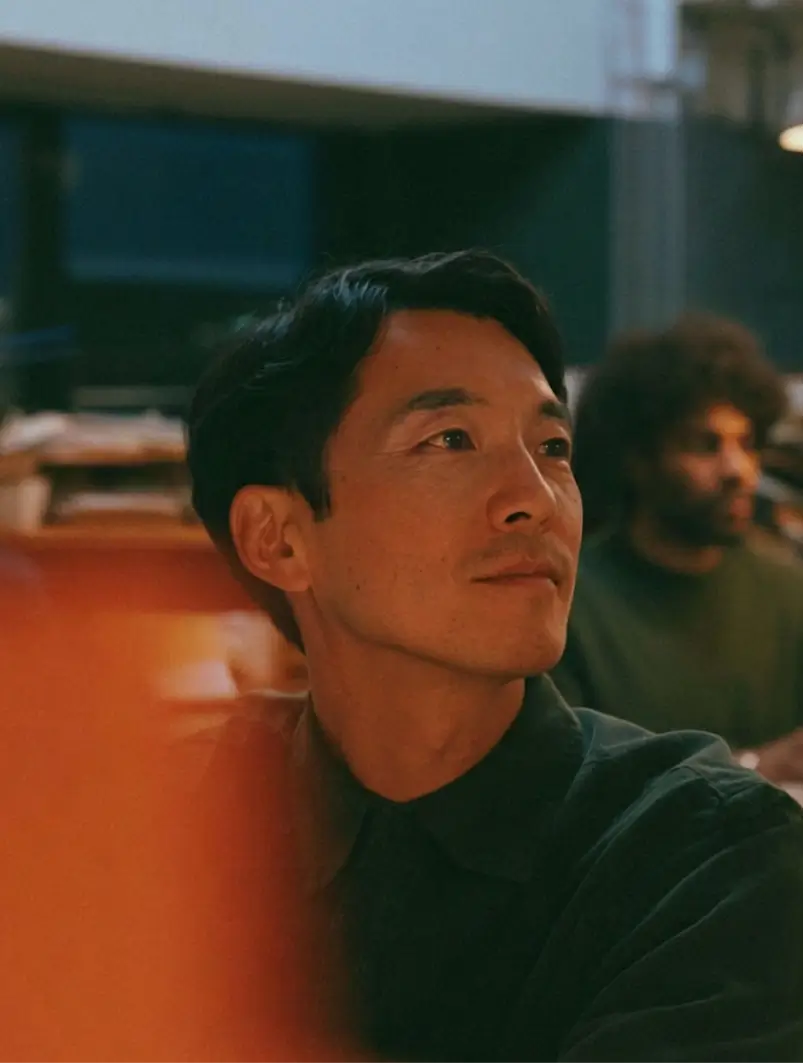 Thoughtful man with short black hair looking to the side in a dimly lit indoor setting.