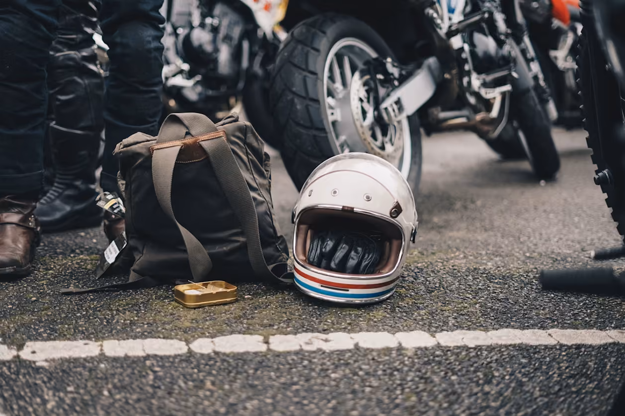 Motorcycle helmet, gloves, and a bag on the ground near a parked motorcycle tire.