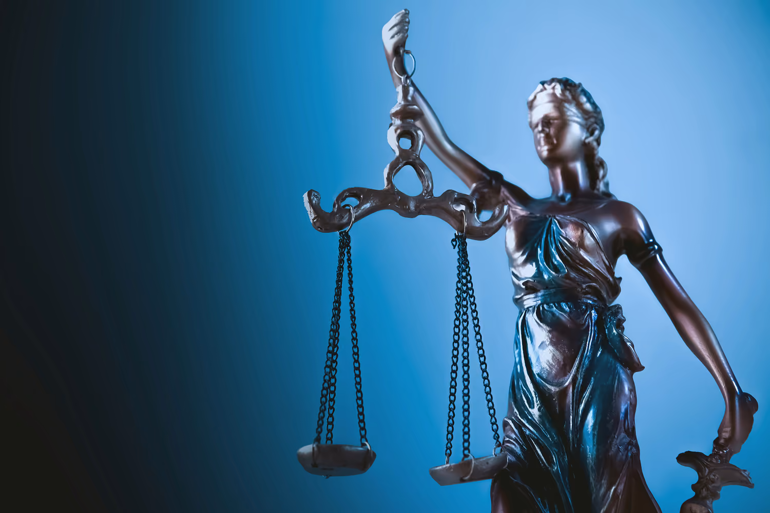Bronze statue of Lady Justice holding balance scales against a blue background.