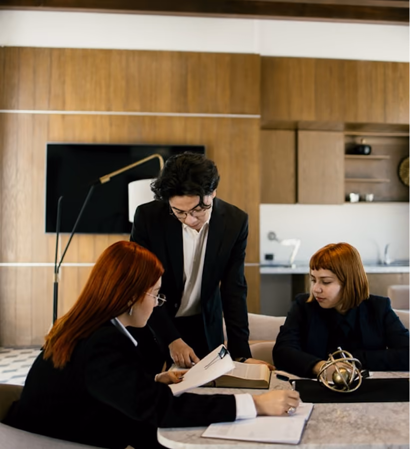 Three business professionals reviewing documents together at a table in an office setting.