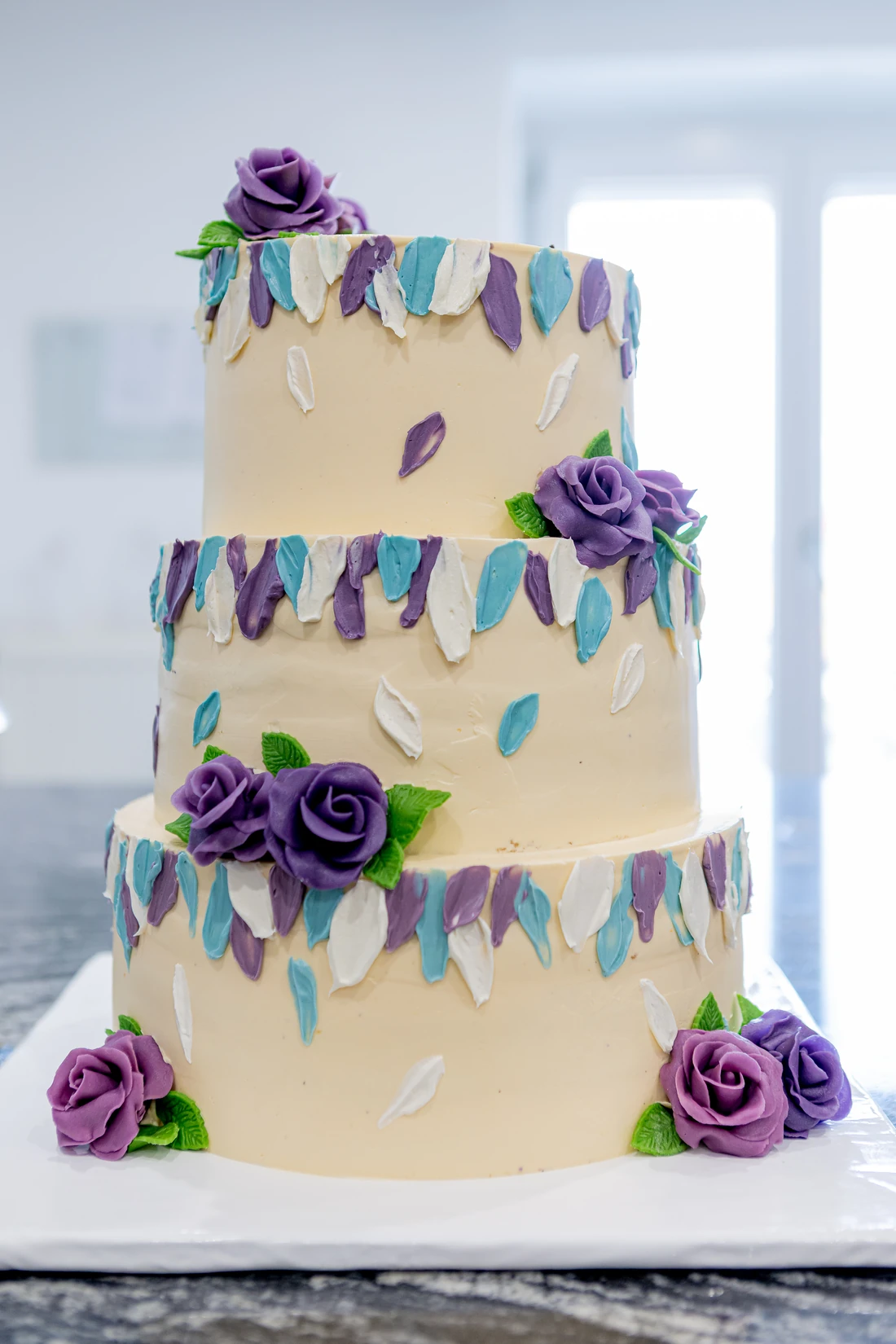 Dreistöckige Hochzeitstorte in Creme mit violetten Zuckerrosen und gemalten Blütenblättern