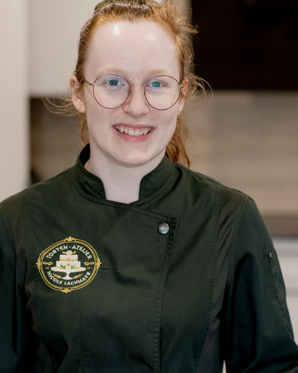 Konditormeisterin Nicole Lachmayr in ihrer dunkelgrünen Kochjacke mit dem Logo des Torten Ateliers