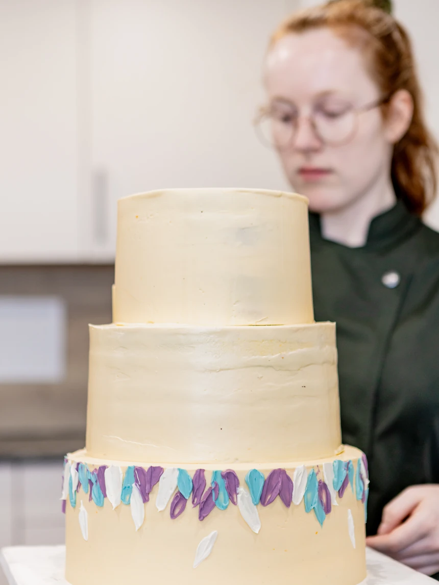 Zweistöckige Torte in Creme mit gemalten Blütenblättern in Violett und Türkis