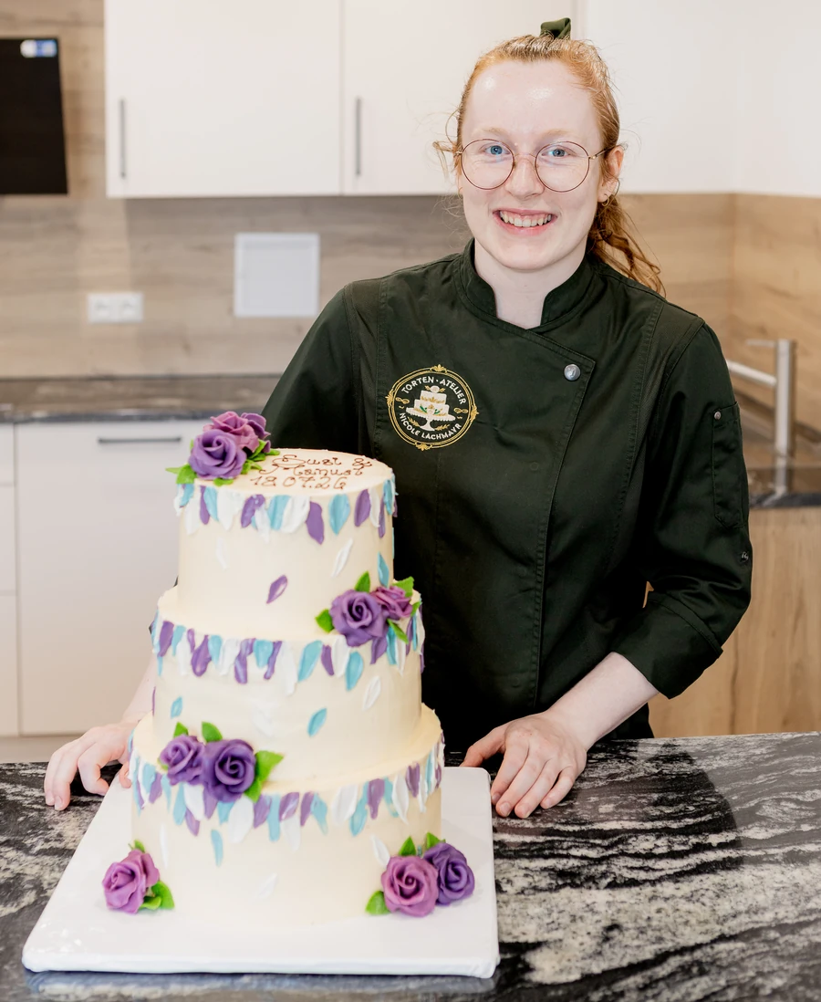 Nicole Lachmayr im Atelier neben ihrer fertigen dreistöckigen Torte mit Rosen und Blütenblättern