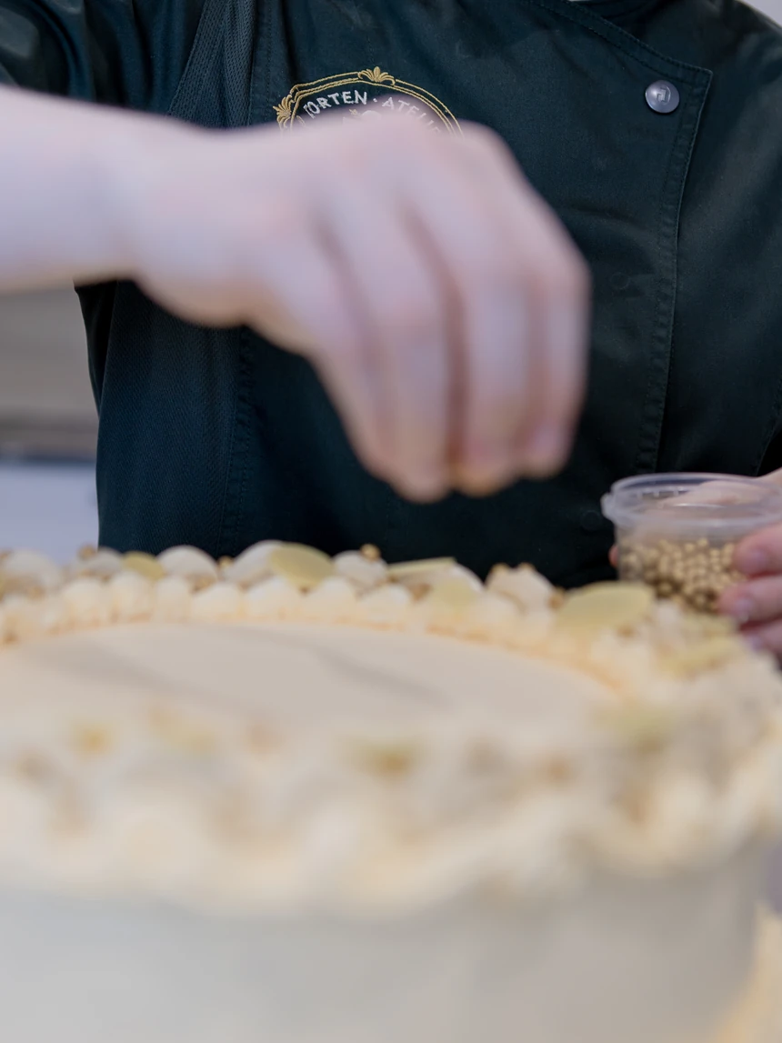 Zuckerperlen werden von Hand auf den Rand einer cremefarbenen Torte gesetzt