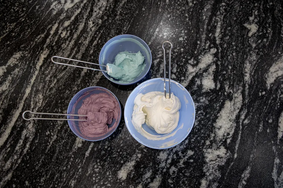 Drei Schalen mit eingefärbter Buttercreme in Mint, Altrosa und Weiß auf dunklem Granit