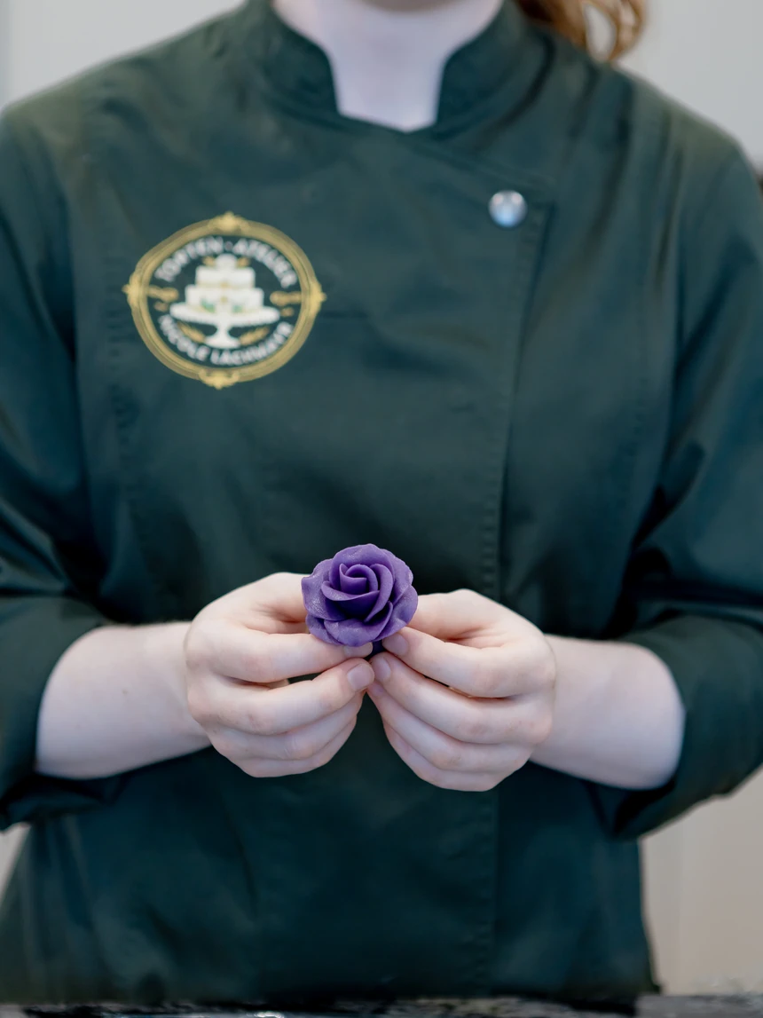 Zwei Hände formen eine violette Zuckerrose vor der dunkelgrünen Kochjacke