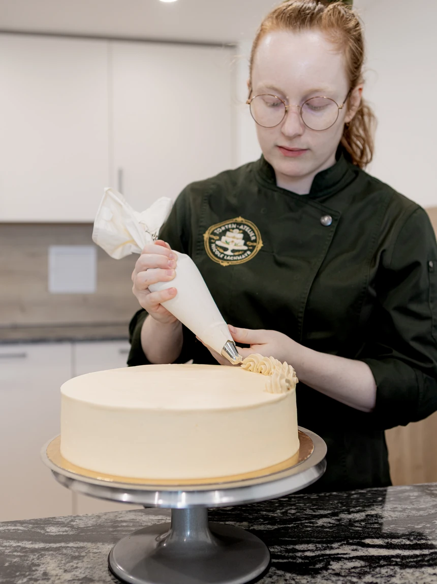 Nicole Lachmayr spritzt mit dem Spritzbeutel eine Borte auf den oberen Rand einer Torte
