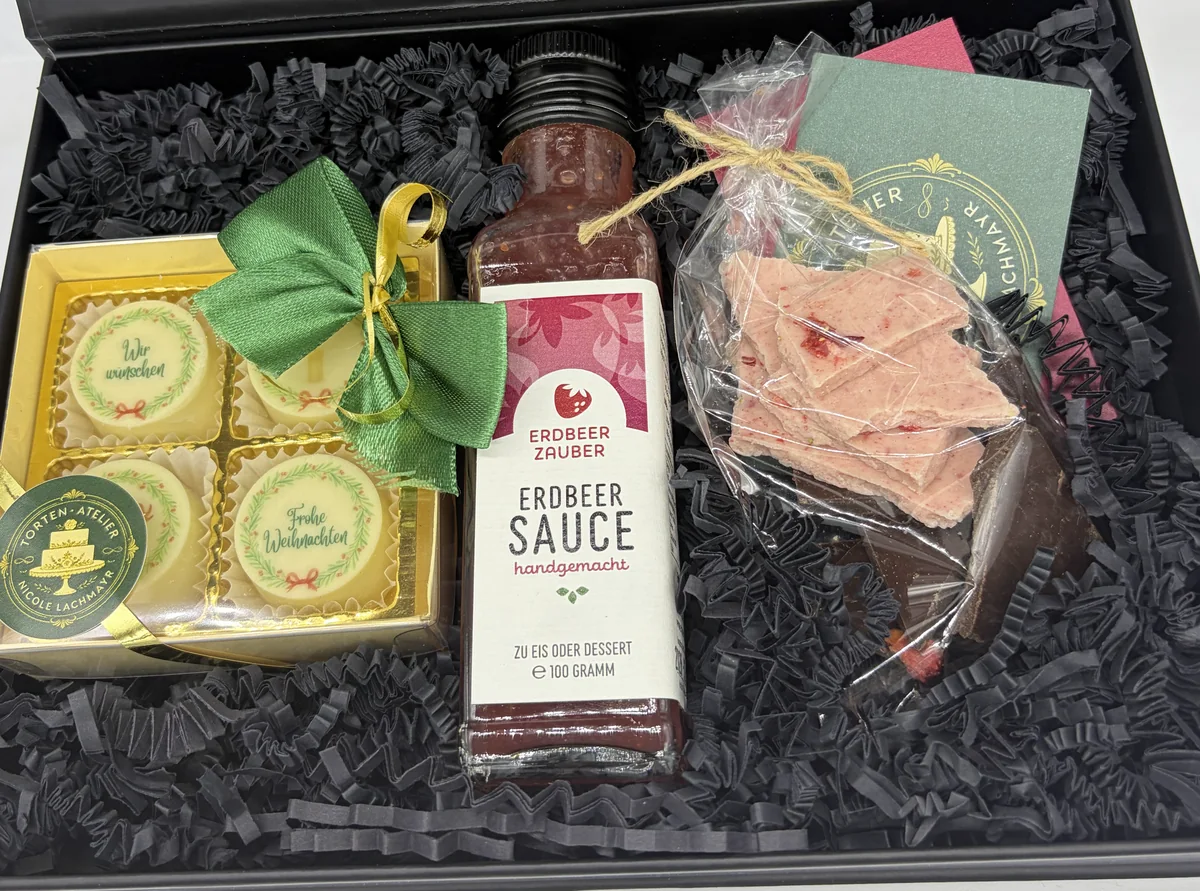 Geschenkset in schwarzer Box: bedruckte Pralinen mit grüner Schleife, eine Flasche Erdbeersauce und Erdbeerschokolade