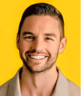 Smiling man with short hair and beard wearing a beige shirt against a yellow background.