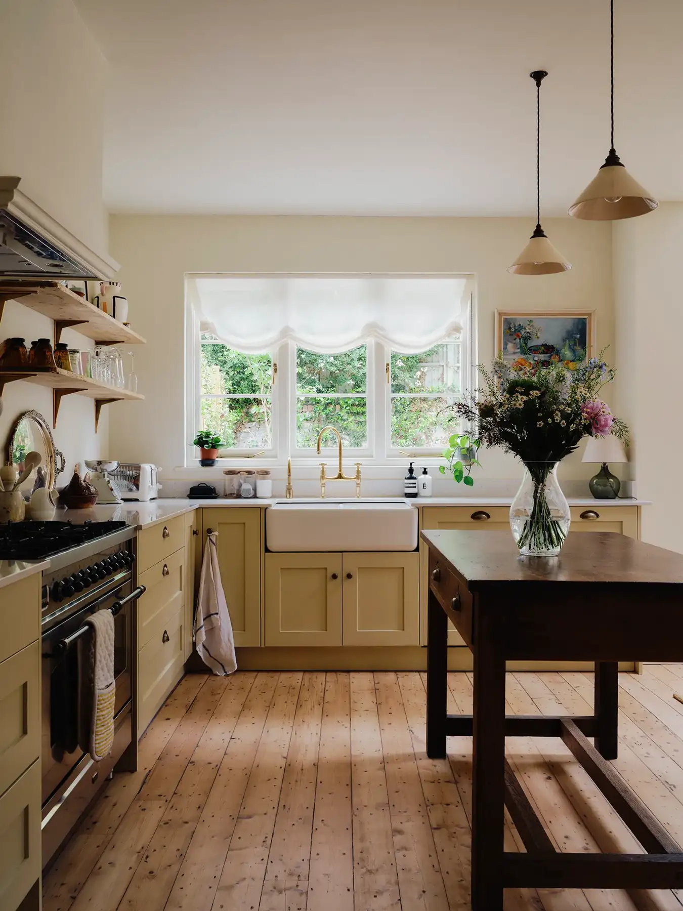 Bright kitchen with yellow cabinets, farmhouse sink, wooden table with flower vase, and large window.