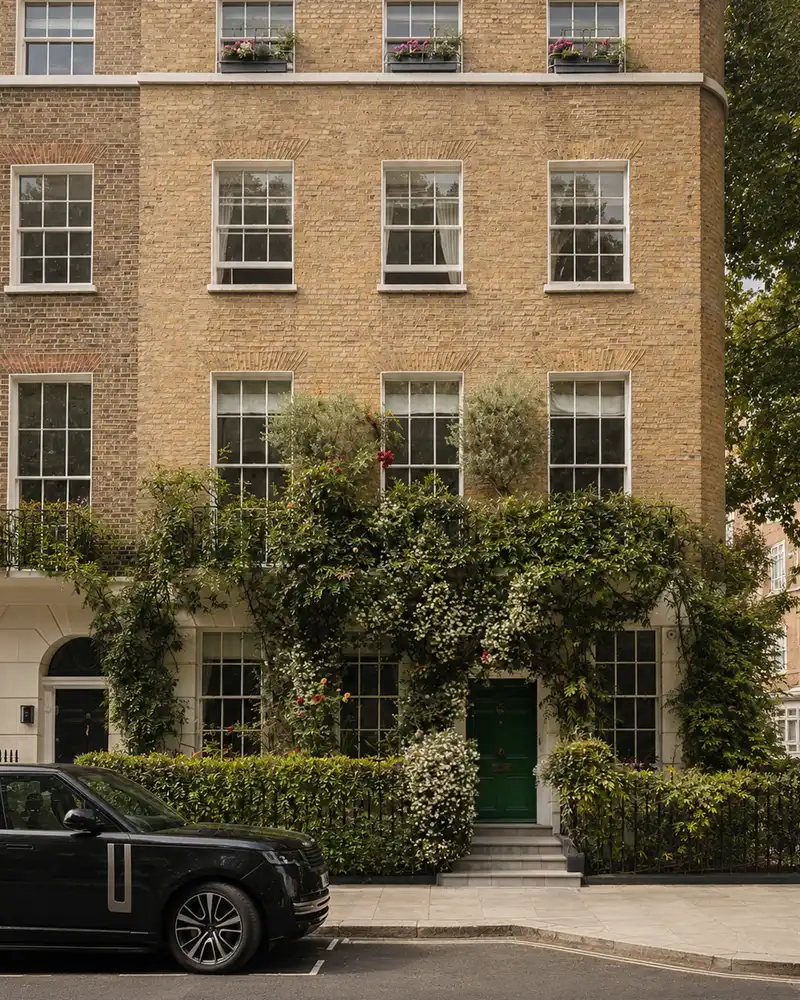 Georgian townhouse facade with green door, climbing plants, and a black car parked outside on street.
