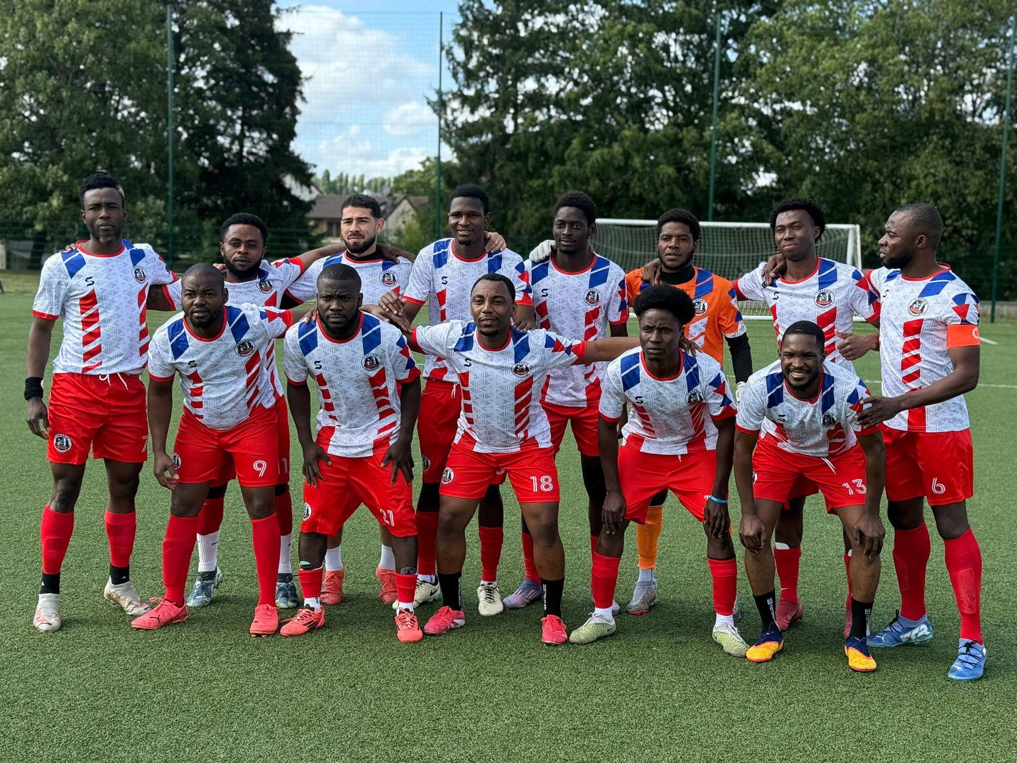 Soccer team in white and red uniforms posing on green field with goal and trees in background.