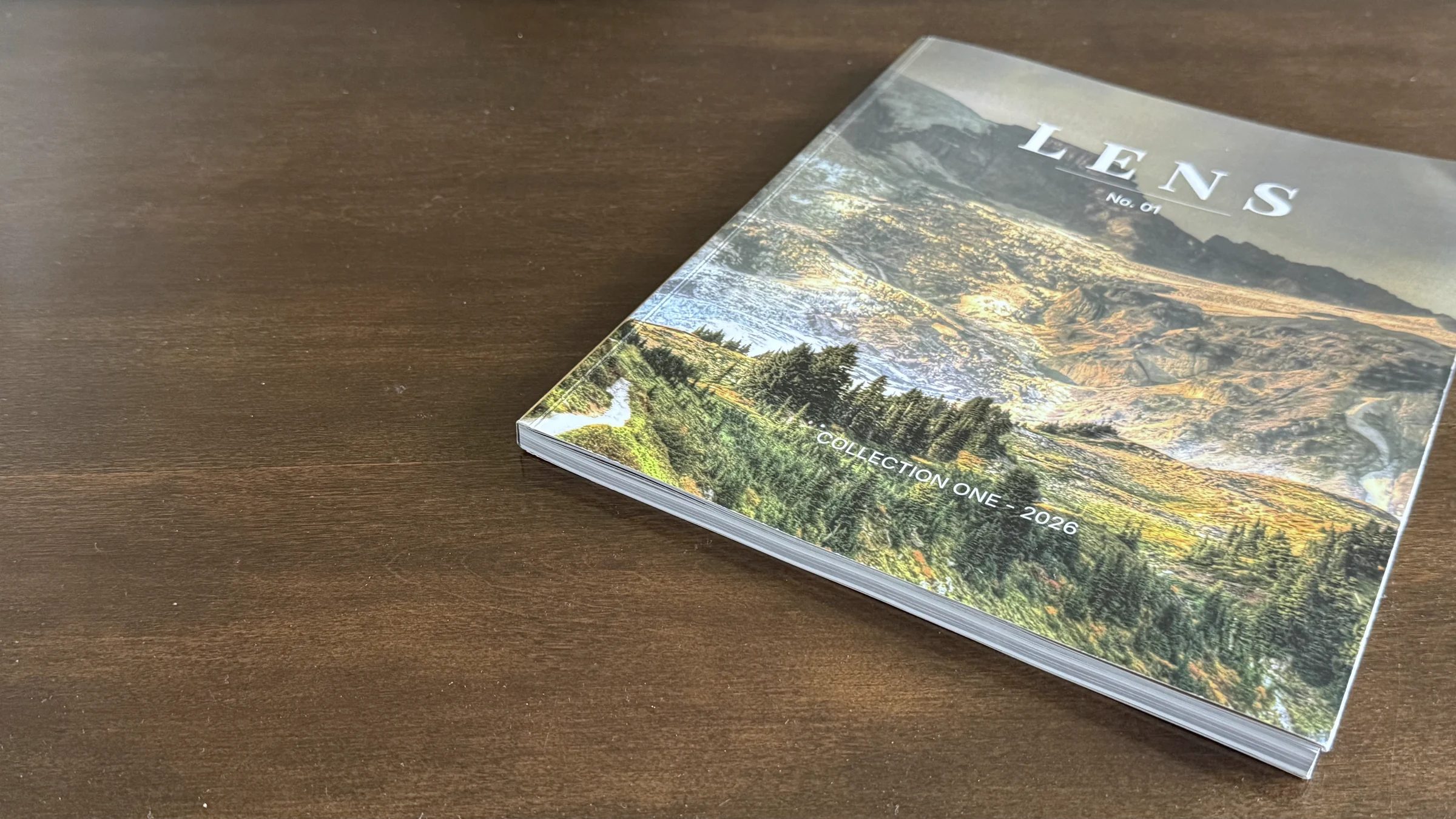 A printed copy of LENS, Collection One, lying on a walnut table.