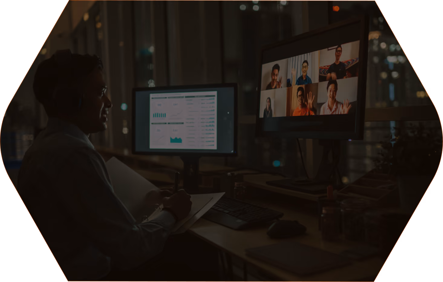 Person with headset participating in a video call with six people on one screen and graphs on another at night.