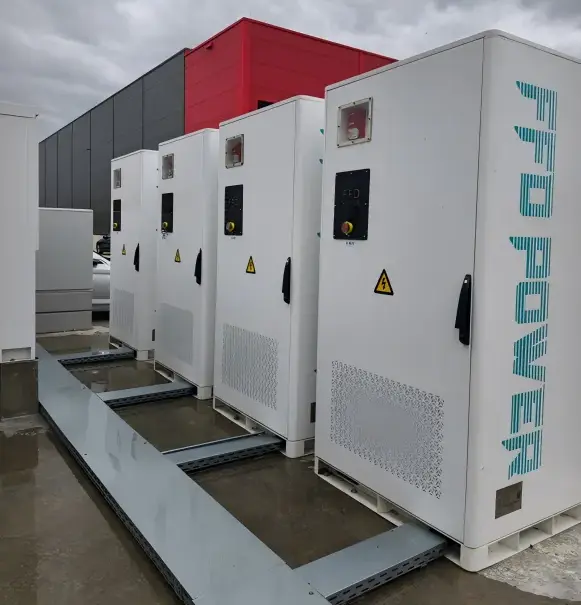 FFD POWER Batterieschränke vor einem Gebäude mit rot-grauer Fassade an einem regnerischen Tag in Deutschland
