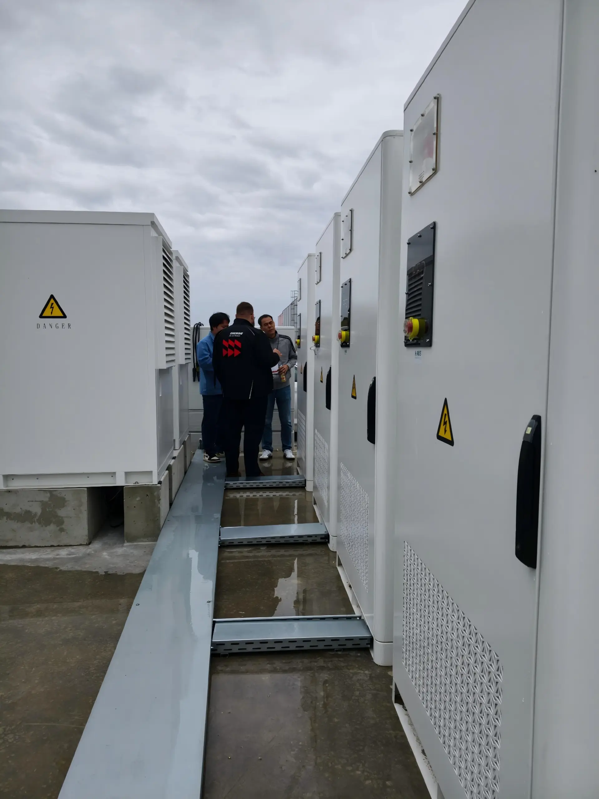 Drei Personen im Gespräch zwischen zwei Reihen von Batterieschränken bei einer Standortbesichtigung