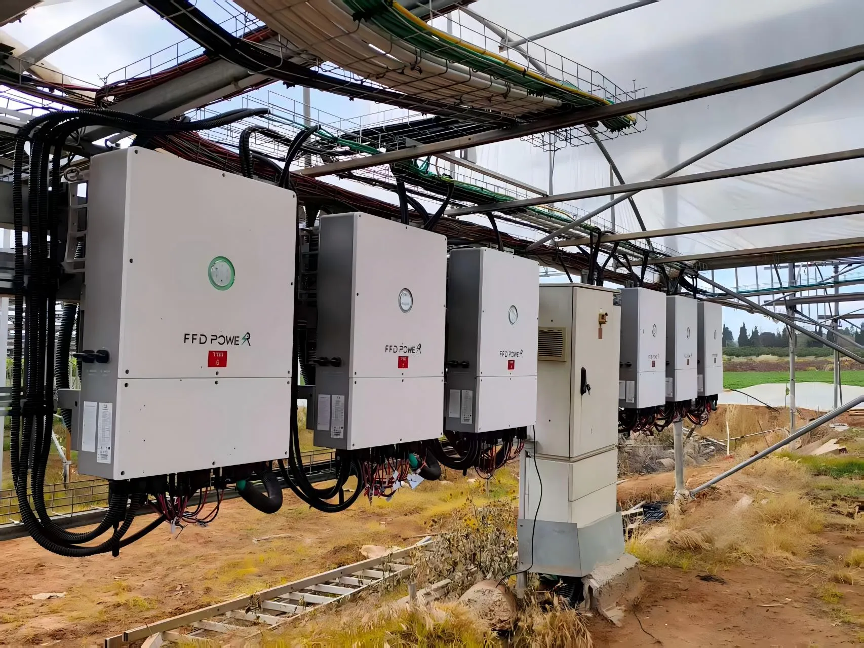 Mehrere wandmontierte FFD POWER Wechselrichter unter einem Gewächshausdach, installiert für ein landwirtschaftliches Solarprojekt