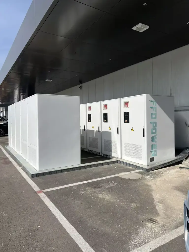 FFD POWER Batterieschränke entlang einer Industriehallen-Außenwand auf unbefestigtem Gelände