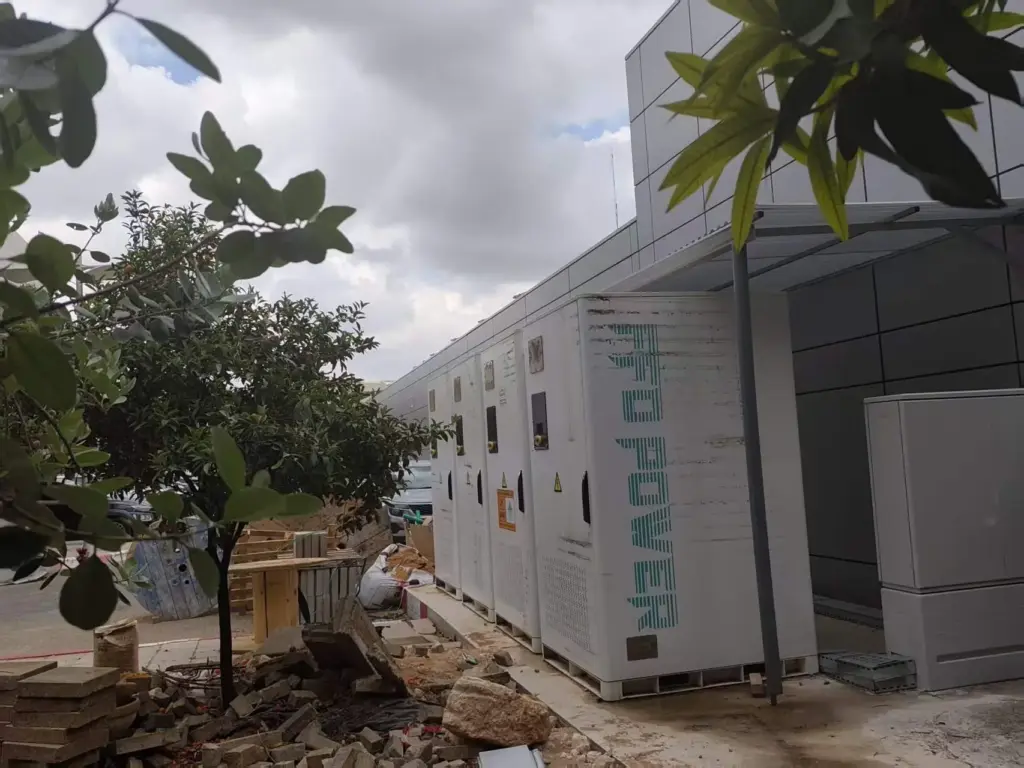 FFD POWER Batterieschränke entlang einer Gewerbegebäude-Fassade an einer Baustelle, im Vordergrund Bäume und Baumaterial