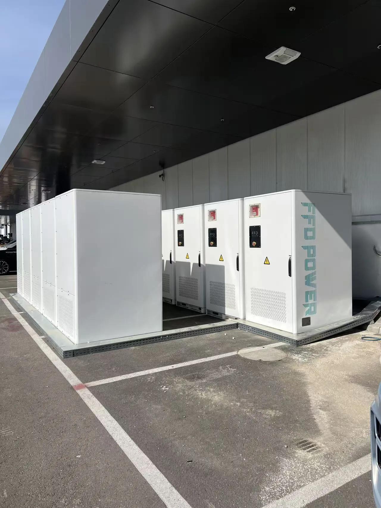 FFD POWER Batterieschränke entlang einer Industriehallen-Außenwand auf unbefestigtem Gelände