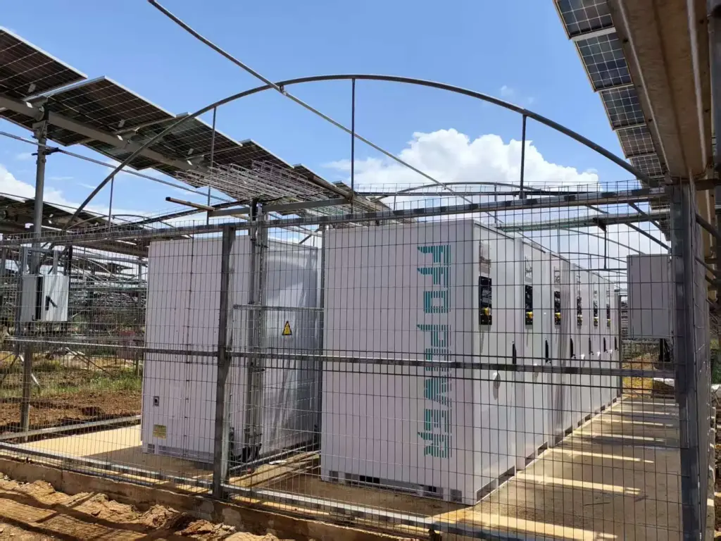 FFD POWER Batterieschränke in einem umzäunten Bereich unter einer PV-Solaranlage auf einem landwirtschaftlichen Gelände