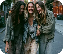 Three young women walking closely on a city street, smiling and enjoying each other's company.
