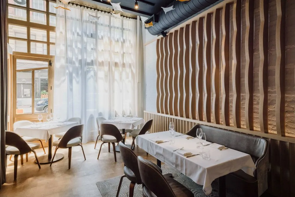 Sunlit dining room at Amphora in Manhattan’s Flatiron District, featuring floor-to-ceiling windows, elegant seating, and contemporary design.
