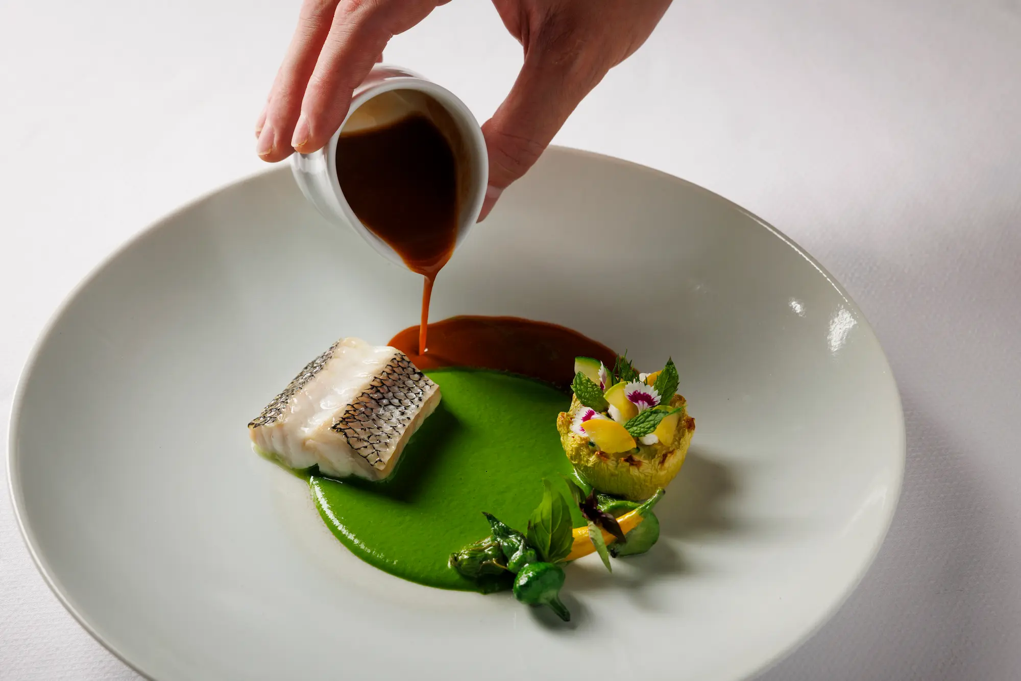 Chef finishing a seasonal seafood course with sauce at Amphora’s wine-first tasting menu restaurant.