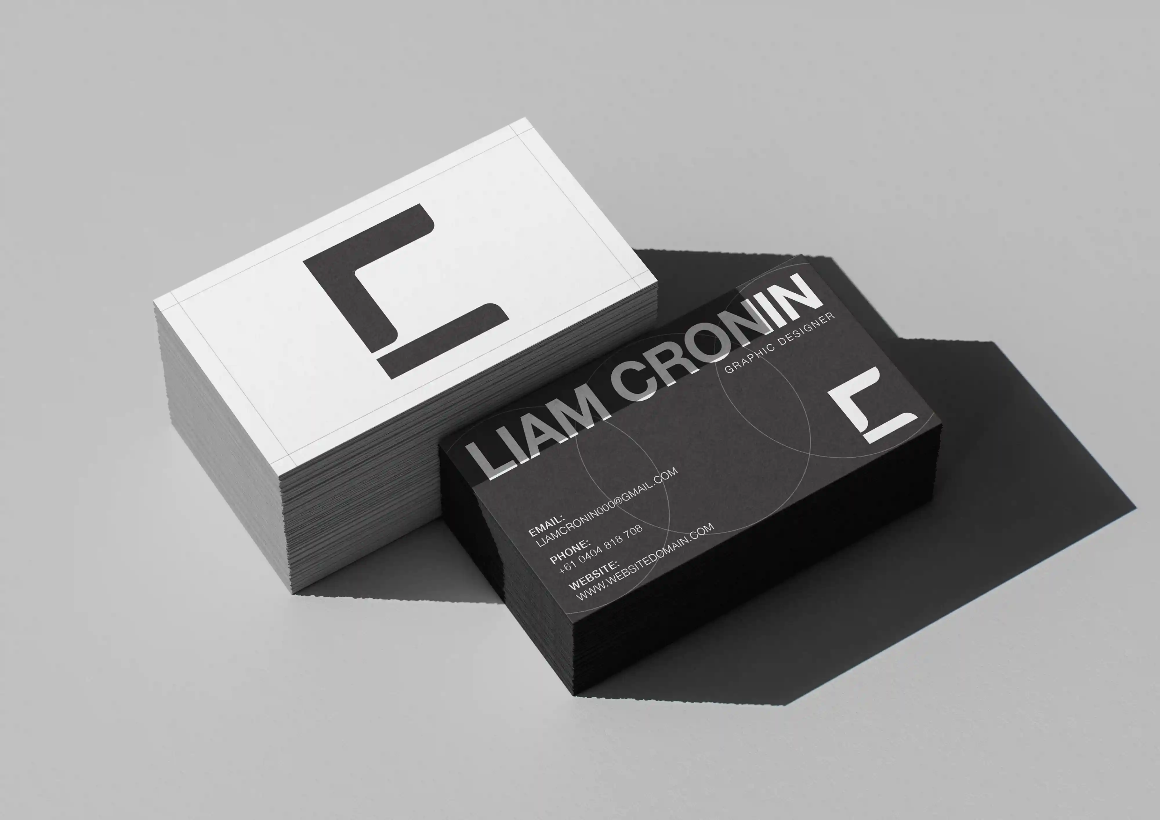 Stacks of black and white business cards for graphic designer Liam Cronin with contact details.
